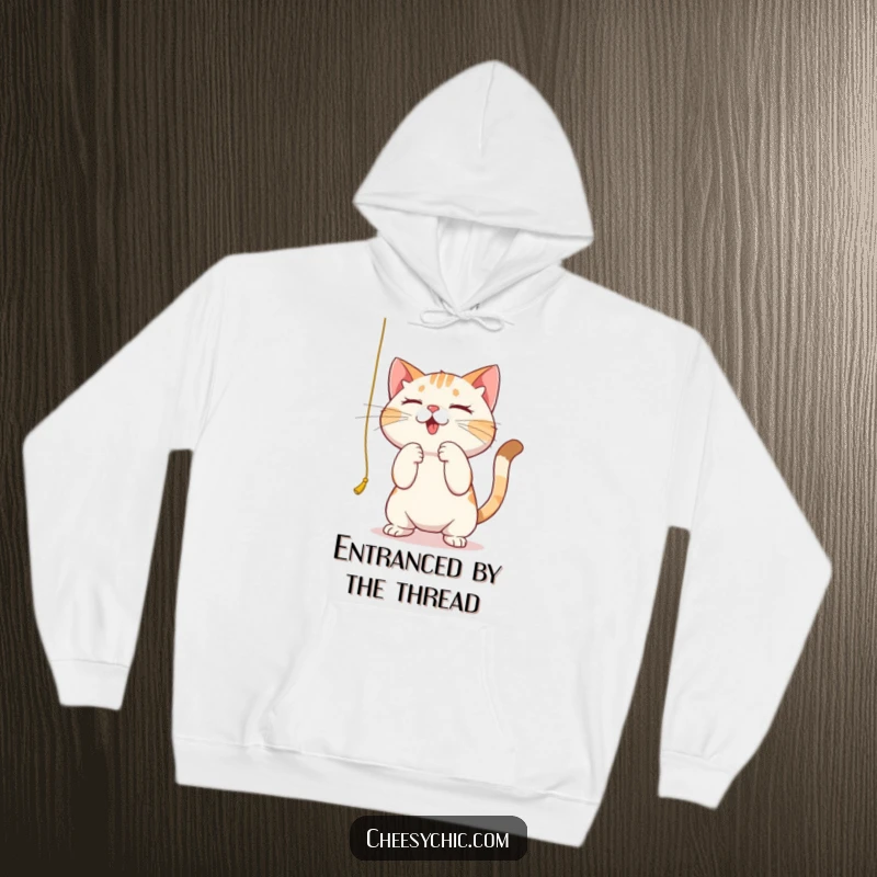 Funny hoodie with a cute cat intensely batting at a hanging string, showing extreme focus and playful dedication.